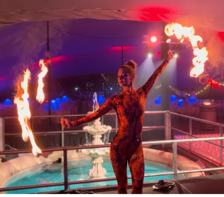 Fire performer with fire fans beside a hotel pool at night